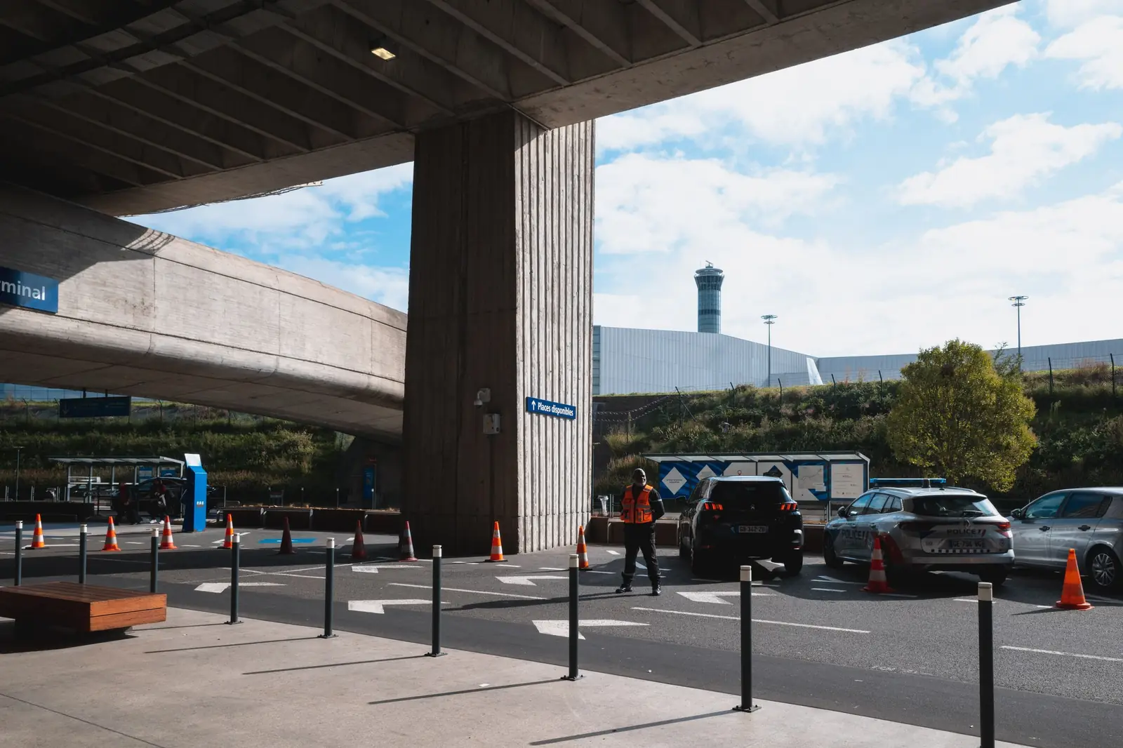 Terminal pick-up road under a concrete overpass with dark cars waiting at the kerb