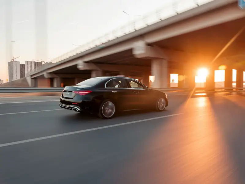 Black Mercedes sedan driving along a highway at sunset