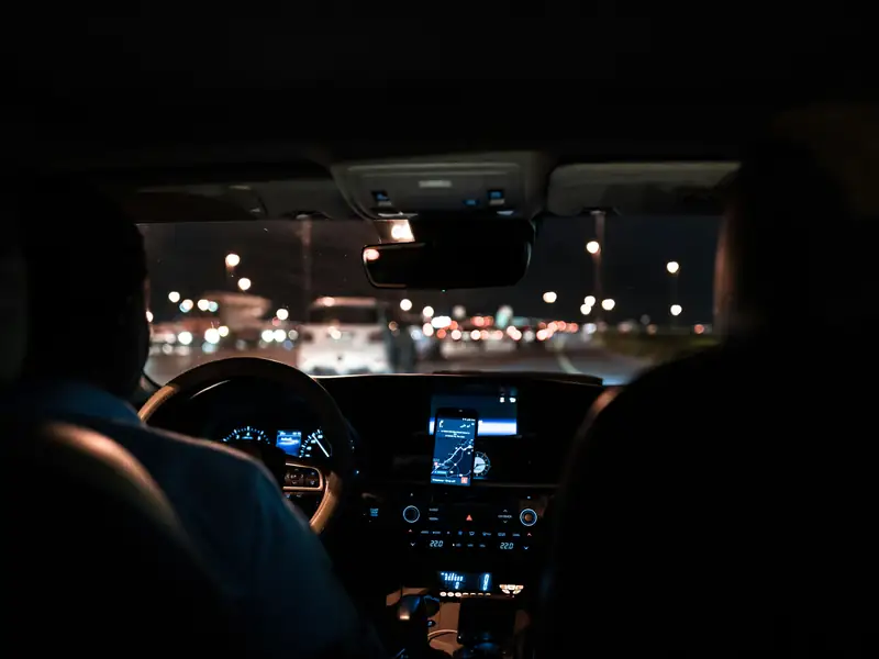 View from the back seat of a car driving through the city at night, with a phone showing the route