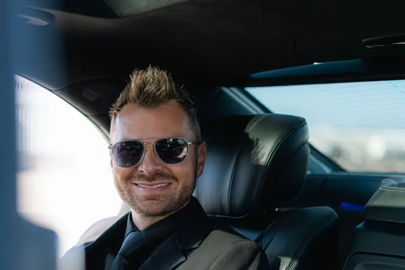 Man in sunglasses smiling in the back of a car
