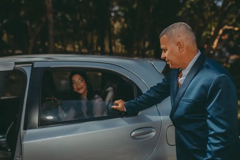 Chauffeur in a blue suit opening the door of a silver car for a passenger