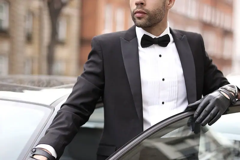 Chauffeur in a tuxedo holding open a car door