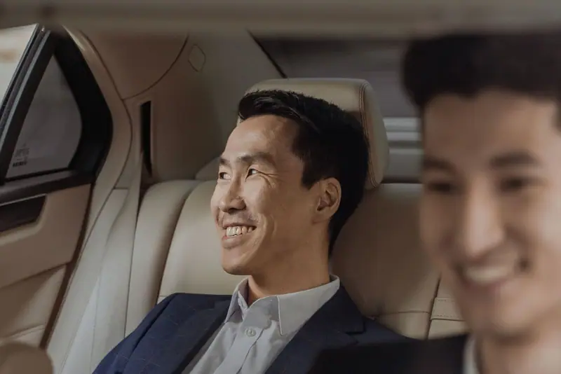 Two businessmen smiling in the back seat of a car