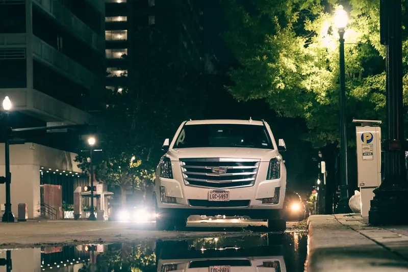 Cadillac Escalade driving on a wet street at night