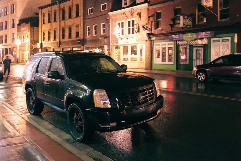 Black Cadillac Escalade on a wet cobbled street at night