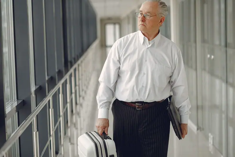 Older businessman with a suitcase in a bright glass corridor