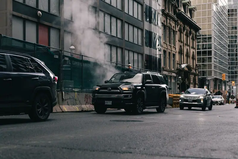 Black SUV waiting at a city intersection with steam rising