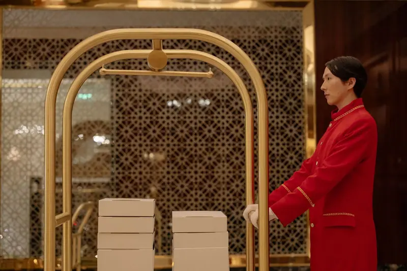 Bellhop in a red uniform with a luggage trolley in a hotel lobby