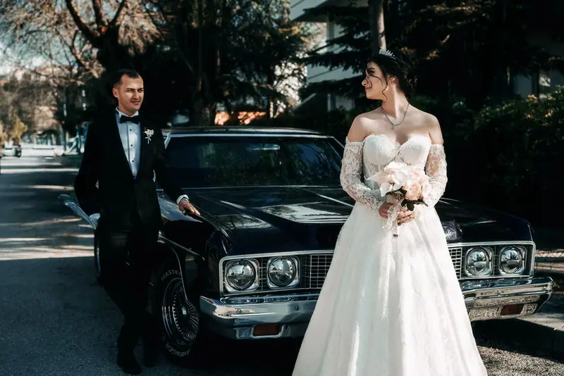 Groom and bride standing beside a classic black car