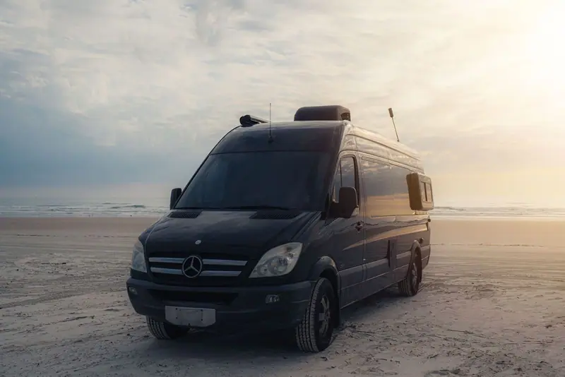 Black Sprinter van parked by the sea at sunset