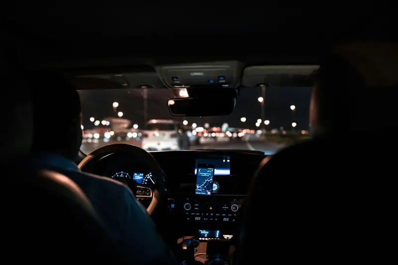 View from the back seat of a car driving through the city at night, with a phone showing the route