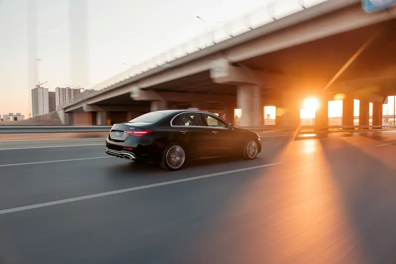 Black Mercedes sedan driving along a highway at sunset