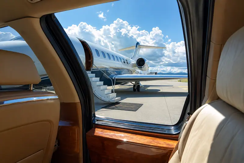Private jet on the apron seen through the open door of a car