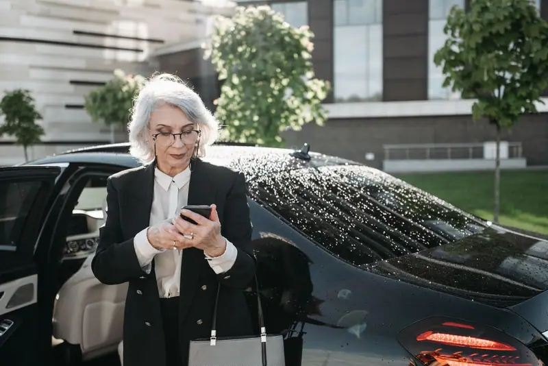 Businesswoman checking her phone beside a black Mercedes-Benz sedan