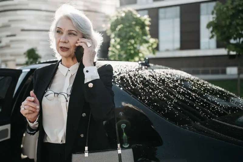 Businesswoman on the phone beside a black Mercedes-Benz sedan with rain on its roof