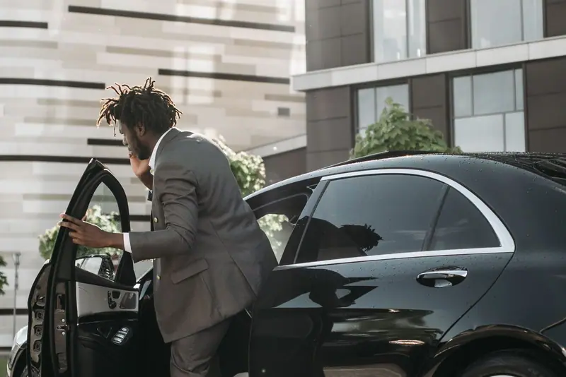 Passenger in a grey suit stepping into a black Mercedes-Benz with the door open