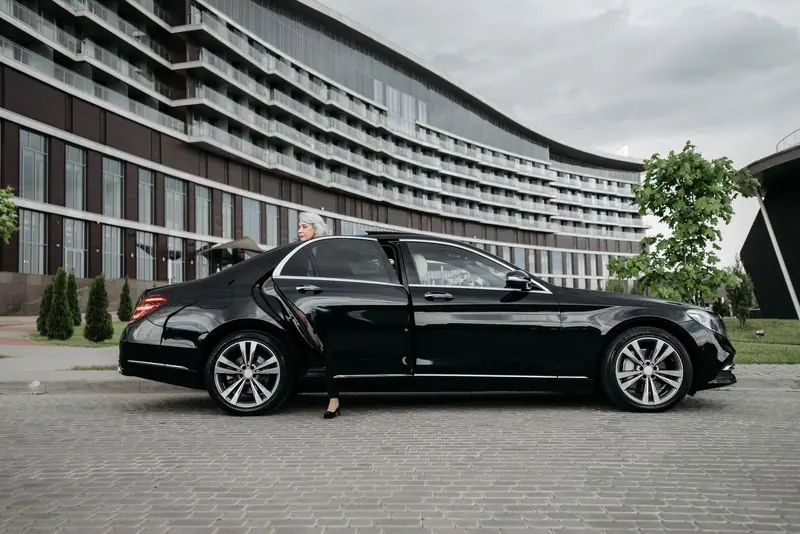 Black Mercedes-Benz S-Class parked in front of a modern hotel with a passenger at the open rear door