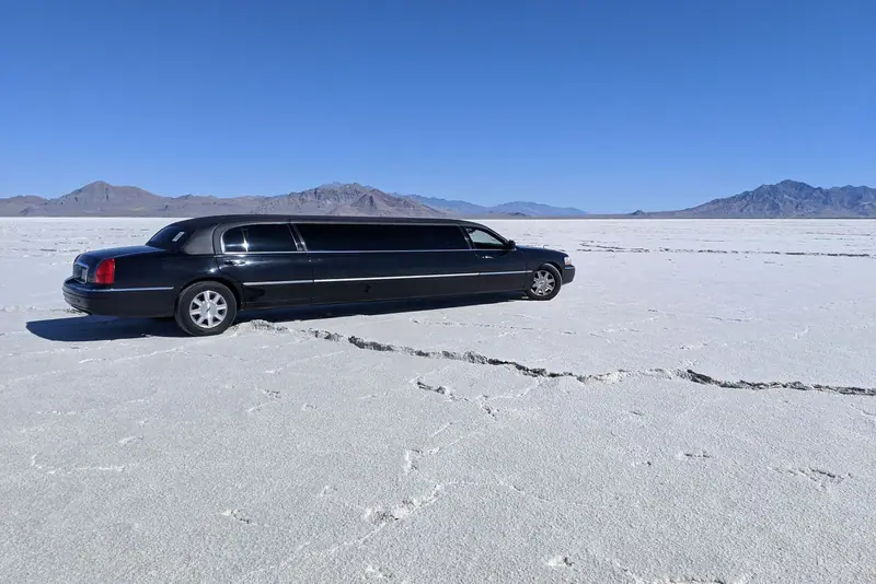 Black stretch limousine parked on a white salt flat with mountains behind