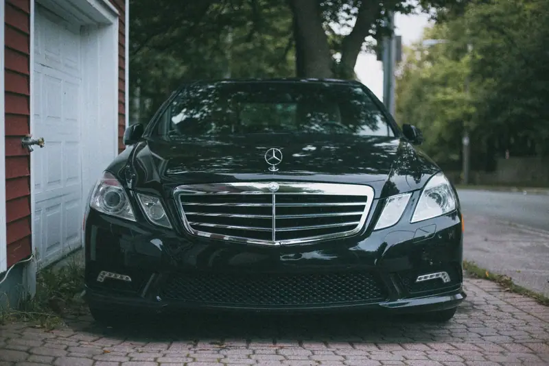 Front of a black Mercedes-Benz E-Class parked beside a white door and trees