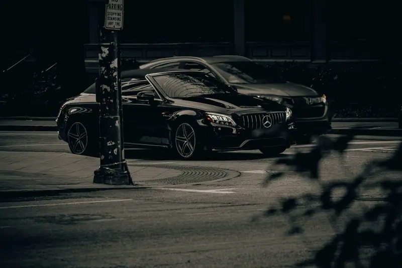 Black Mercedes-Benz car parked on a dark city street at night beside a lamp post