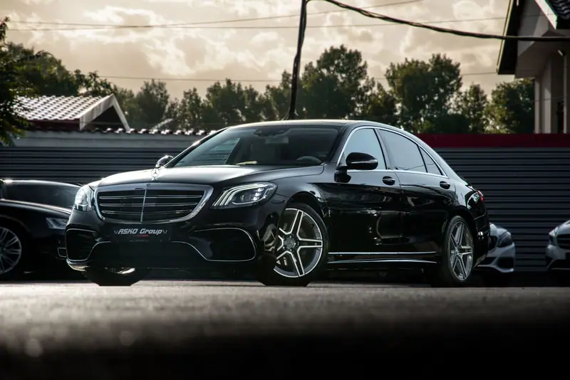 Black Mercedes-Benz S-Class sedan parked in a car park with trees behind
