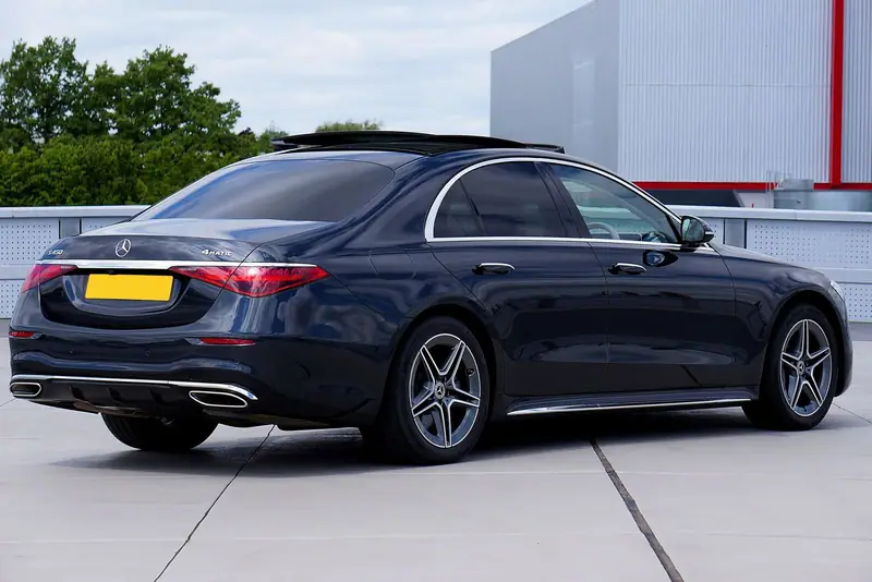 Dark blue Mercedes-Benz S-Class sedan seen from behind, parked in front of a white building
