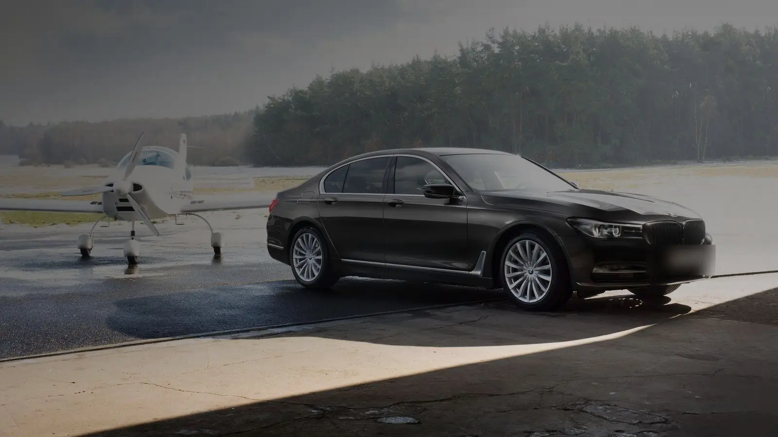 Black BMW 7 Series sedan parked on an airport apron beside a small plane