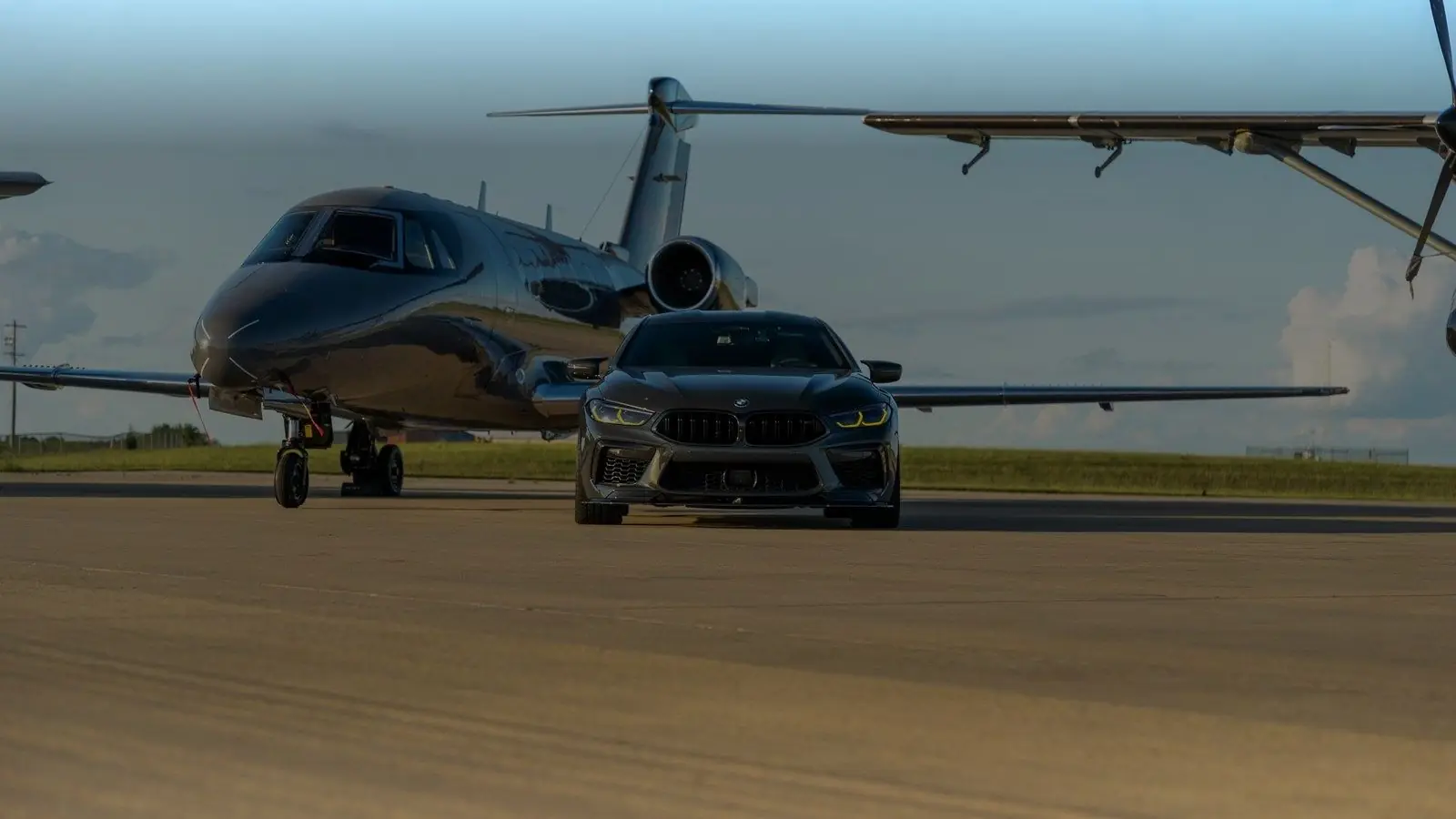 Dark BMW sedan parked in front of a private jet on an airport apron