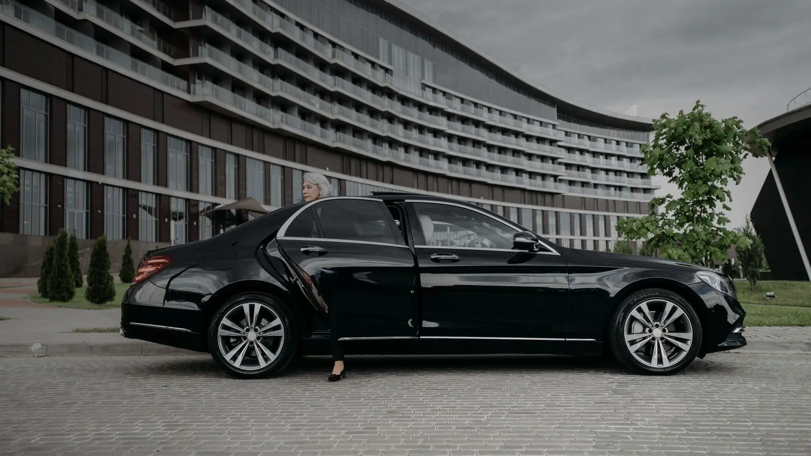 Black Mercedes-Benz S-Class parked in front of a modern hotel with a passenger at the open rear door