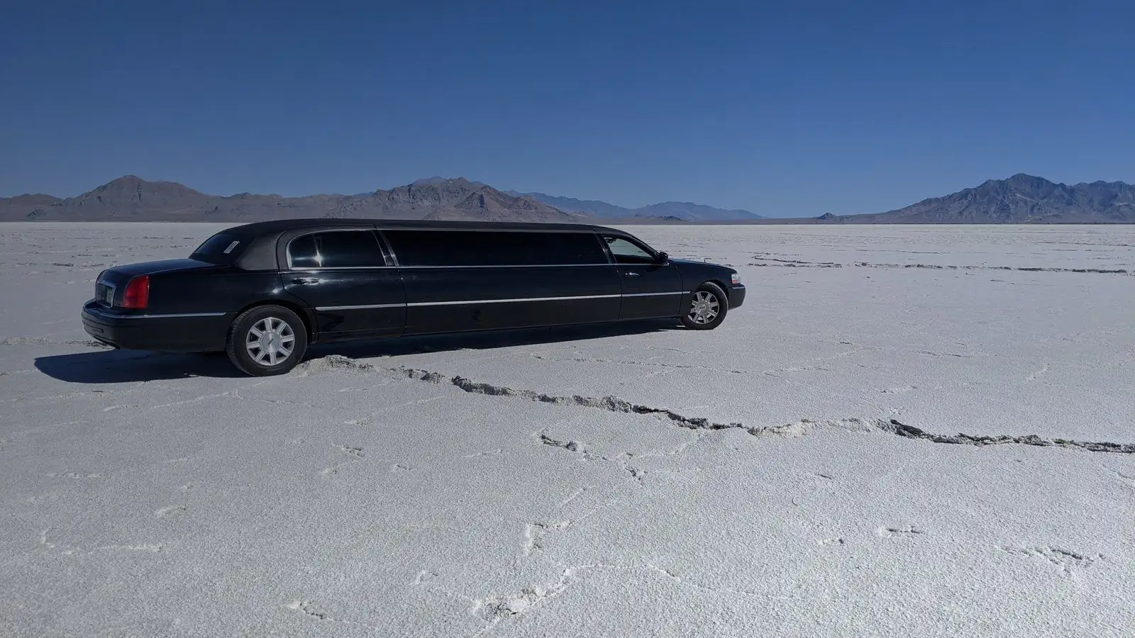 Black stretch limousine parked on a white salt flat with mountains behind