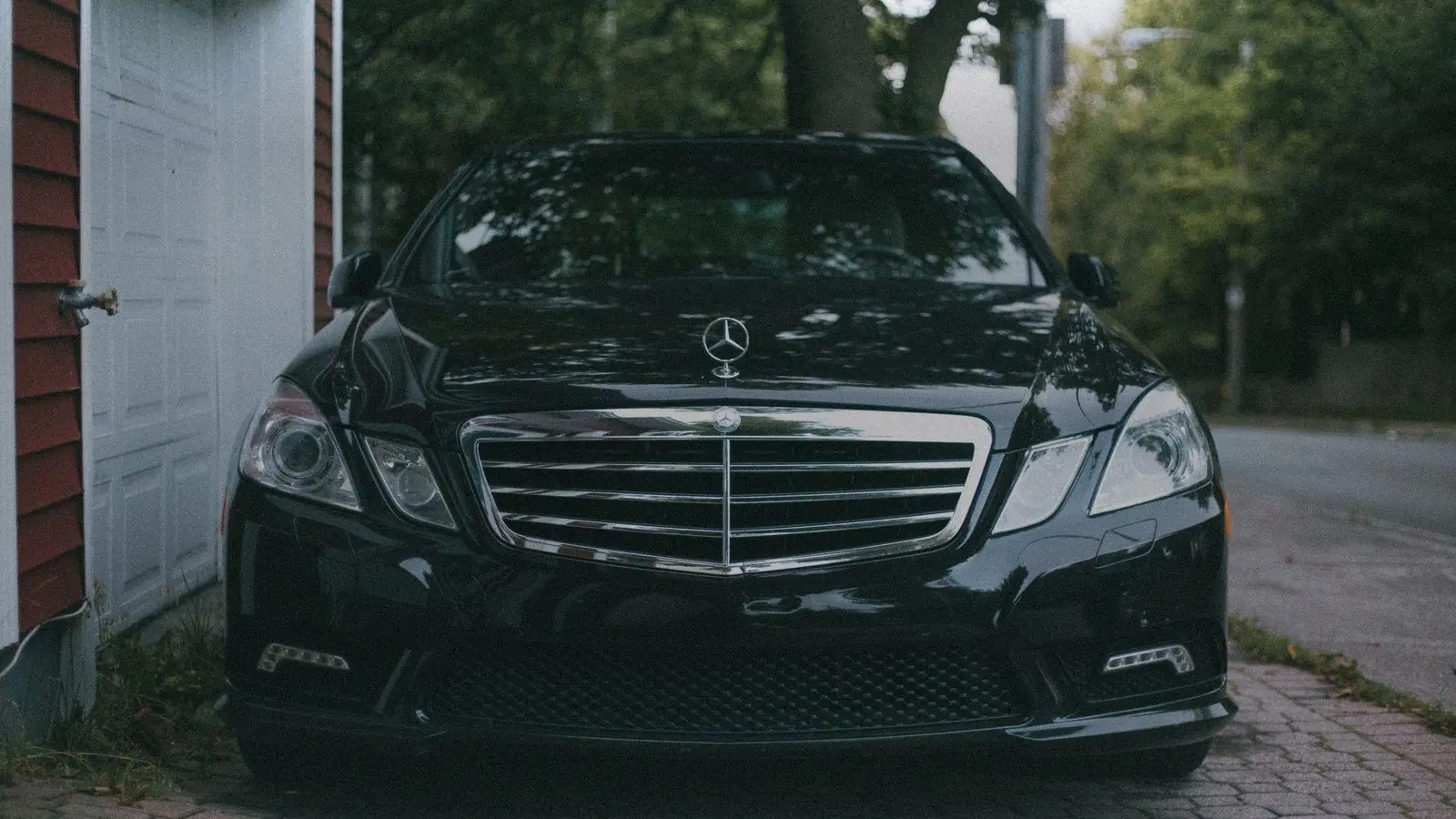 Front of a black Mercedes-Benz E-Class parked beside a white door and trees