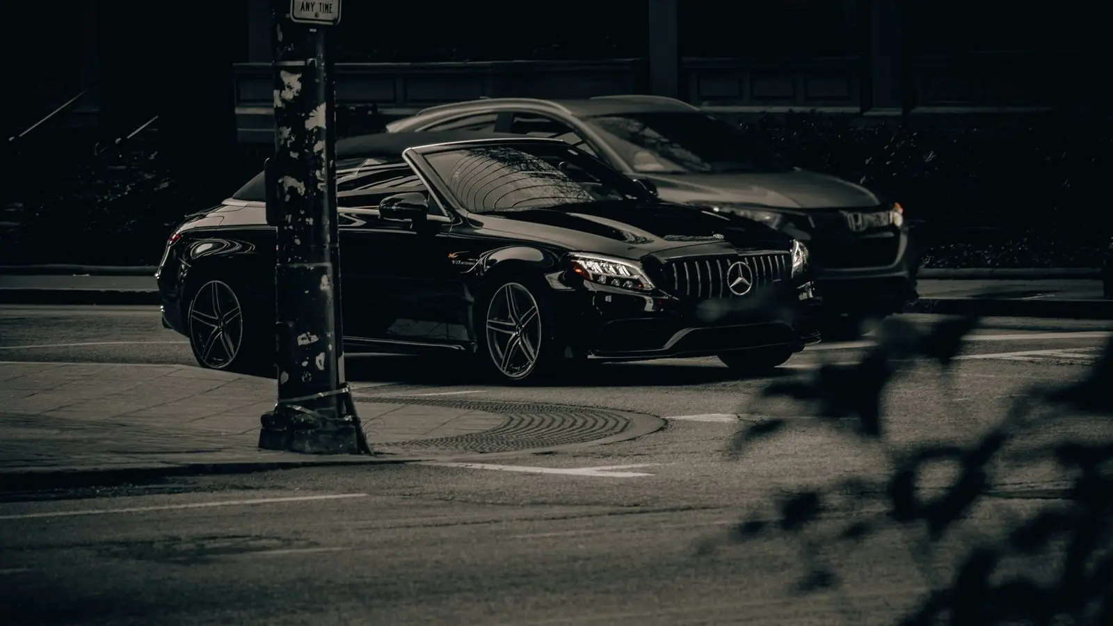 Black Mercedes-Benz car parked on a dark city street at night beside a lamp post