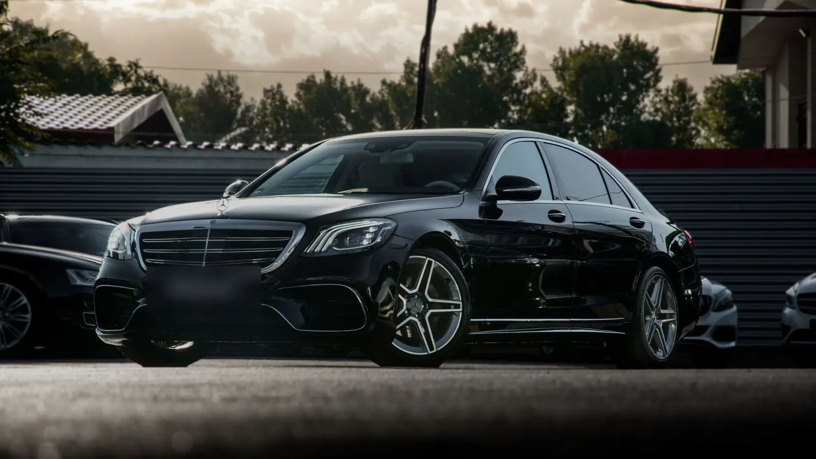 Black Mercedes-Benz S-Class sedan parked in a car park with trees behind