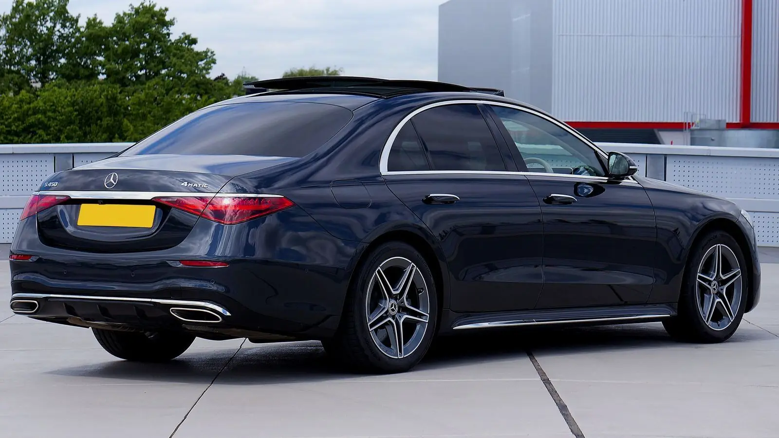 Dark blue Mercedes-Benz S-Class sedan seen from behind, parked in front of a white building